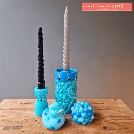 Voorbeeld van Vrolijke mix in blauwtinten: beschilderde cilinder met kandelaar, kandelaartje, badeendje en bolletjes ornament op houten tafel